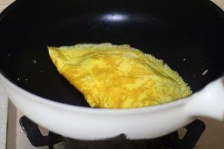 Omelette Fried Rice step 19: Fold the omelette over the rice, shape it neatly, and cook briefly to seal.